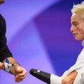 A female para athlete watches as her coach approaches with a prosthesis for her fencing competition. 